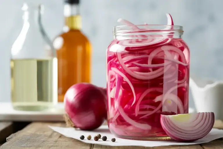 A jar of vibrant pickled red onions, with bottles of the best vinegar types like white and apple cider vinegar nearby.