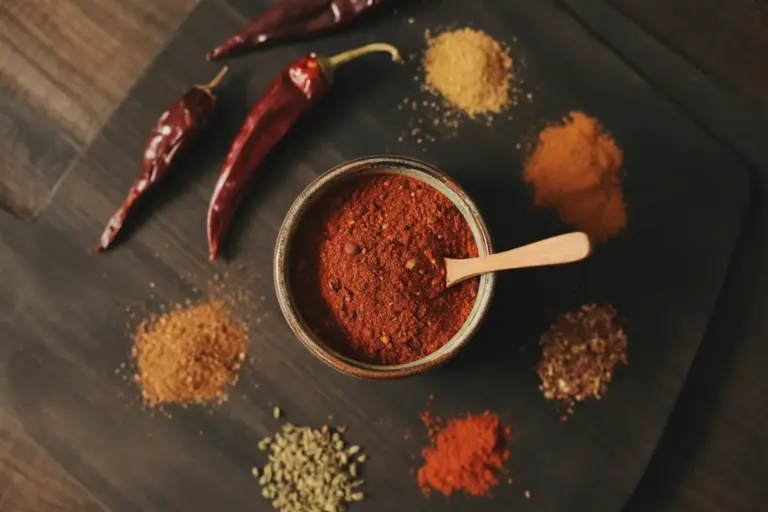 A rustic bowl of homemade DIY chili seasoning mix surrounded by its core ingredients like dried chili peppers, cumin, and paprika on a wooden table.