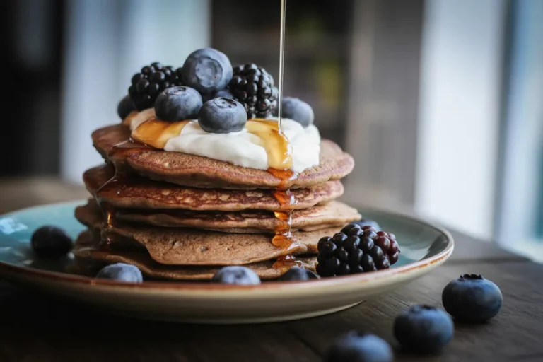 A healthy stack of gluten-free pancakes made with just buckwheat flour, topped with fresh berries, yogurt, and maple syrup.