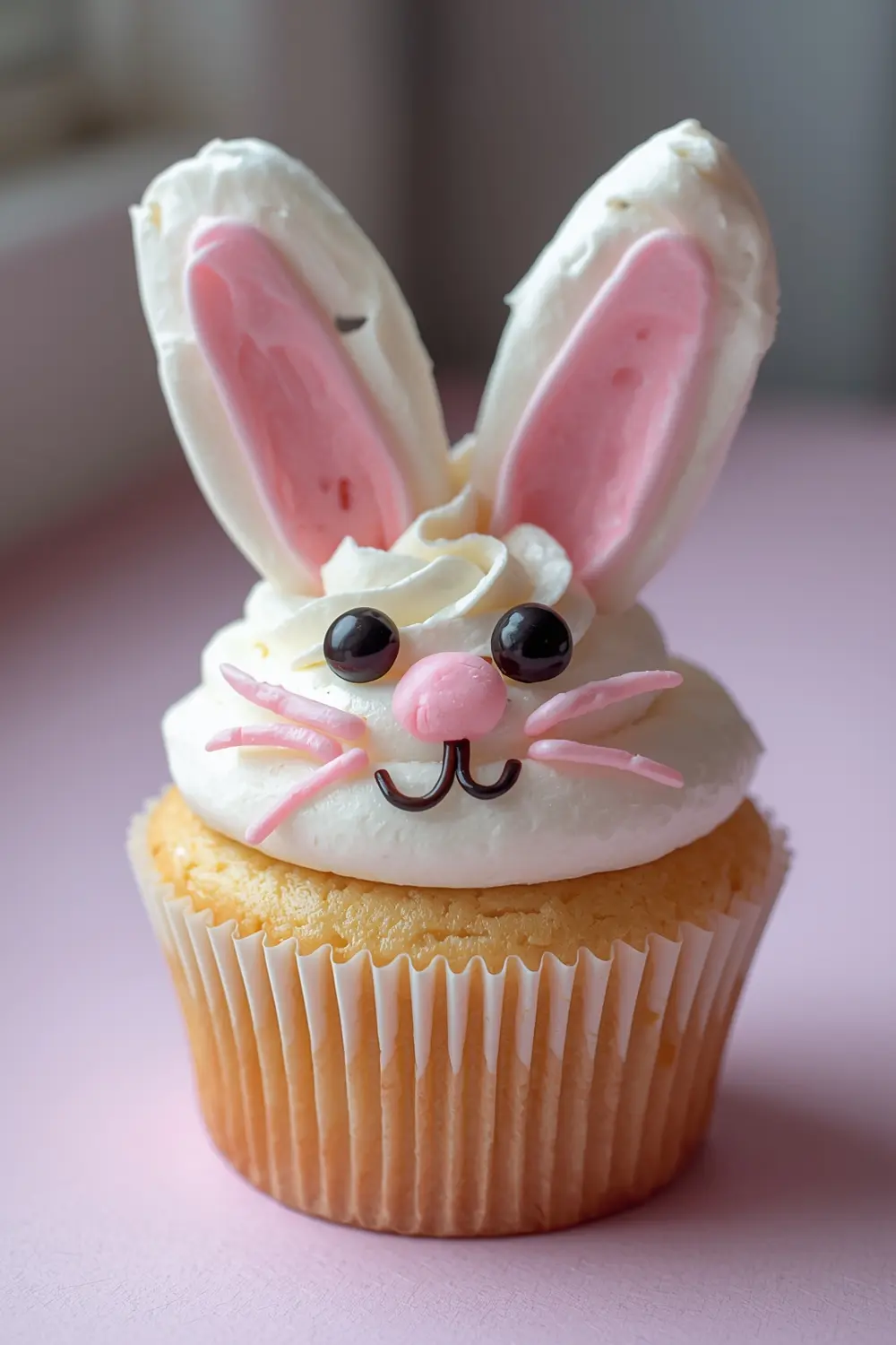 A close-up photo of a bunny-themed cupcake with marshmallow ears and colorful candy melt details