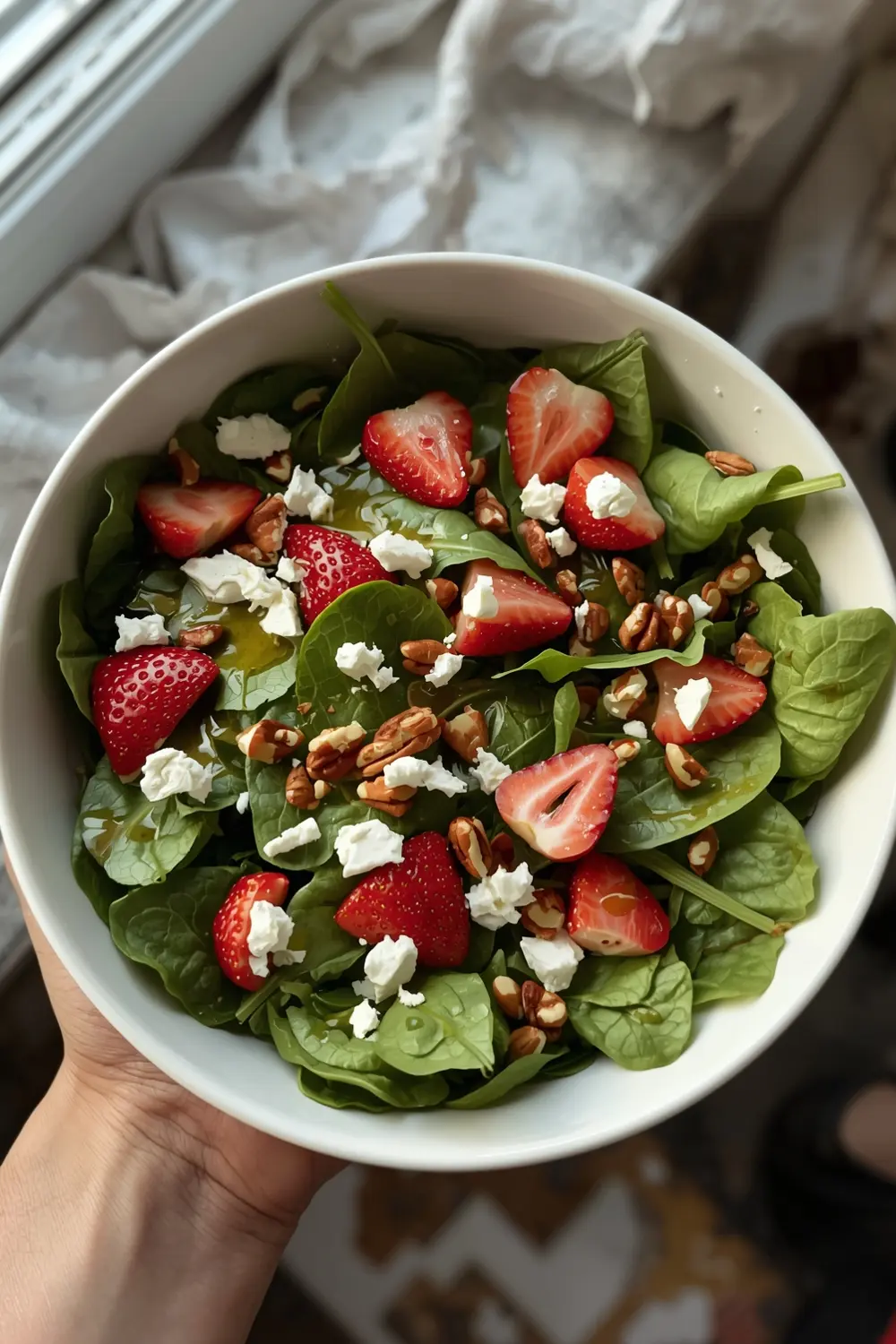 A colorful salad with spinach, strawberries, feta cheese, and pecans