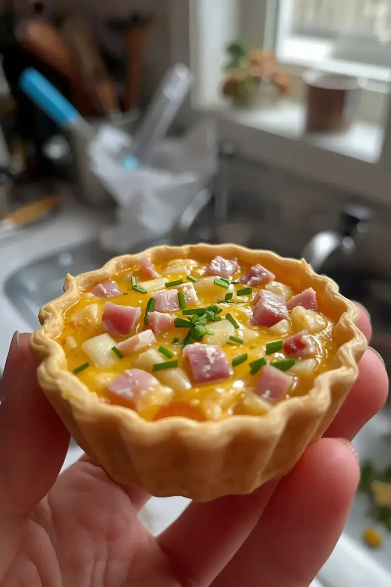 A photo of a mini quiche with melted cheese, ham, and parsley