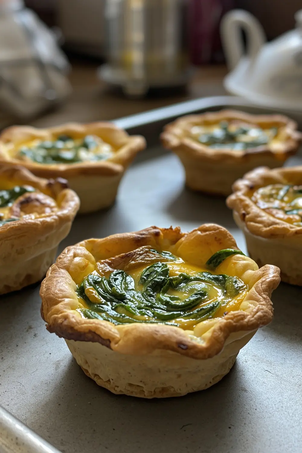 A photo of mini spinach quiches on a baking sheet, fresh from the oven.